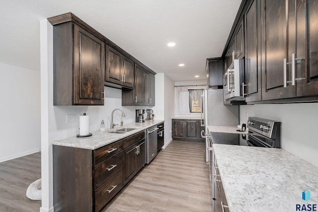 kitchen with dark brown cabinets, appliances with stainless steel finishes, light wood-style floors, and a sink