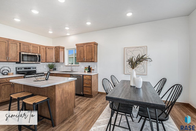 kitchen with dark wood finished floors, light countertops, appliances with stainless steel finishes, a kitchen breakfast bar, and a sink