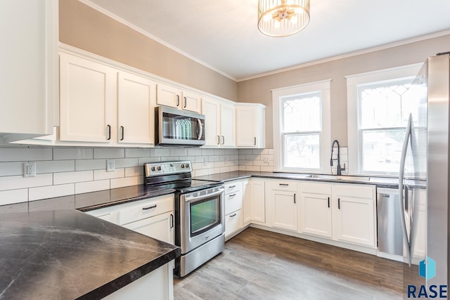 kitchen with dark countertops, ornamental molding, appliances with stainless steel finishes, and a sink