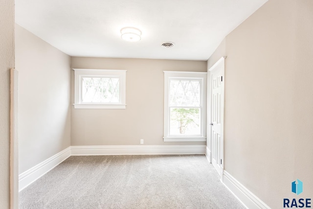 carpeted spare room featuring a wealth of natural light, visible vents, and baseboards