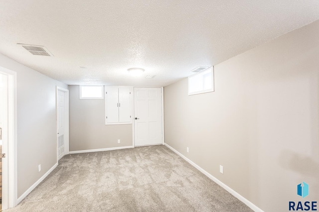 below grade area with light carpet, visible vents, a textured ceiling, and baseboards