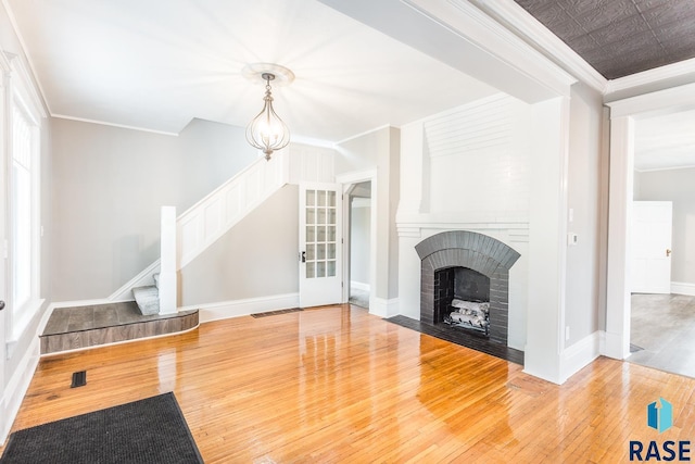 living area with stairway, baseboards, a fireplace, wood-type flooring, and crown molding