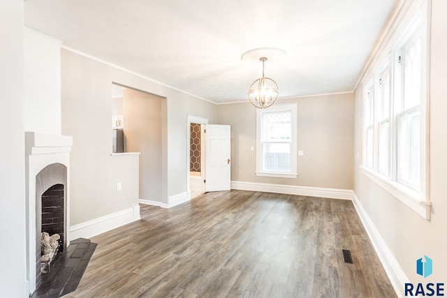 unfurnished living room with visible vents, a notable chandelier, ornamental molding, wood finished floors, and baseboards