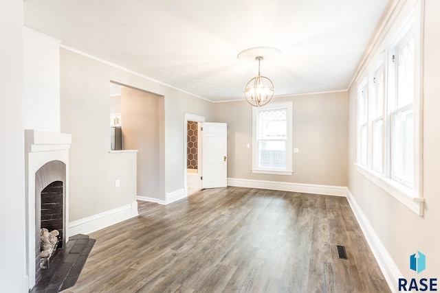 unfurnished living room with visible vents, a notable chandelier, ornamental molding, wood finished floors, and baseboards
