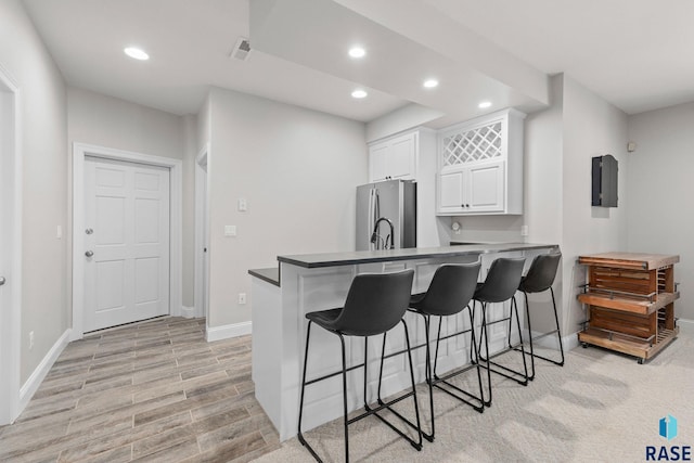 kitchen featuring a breakfast bar area, a peninsula, recessed lighting, freestanding refrigerator, and white cabinetry