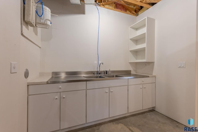 kitchen featuring open shelves, concrete floors, stainless steel countertops, white cabinetry, and a sink