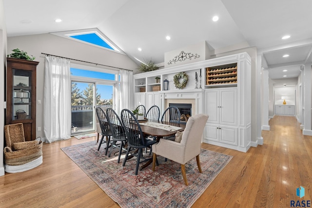 dining space featuring lofted ceiling, a glass covered fireplace, recessed lighting, light wood finished floors, and baseboards