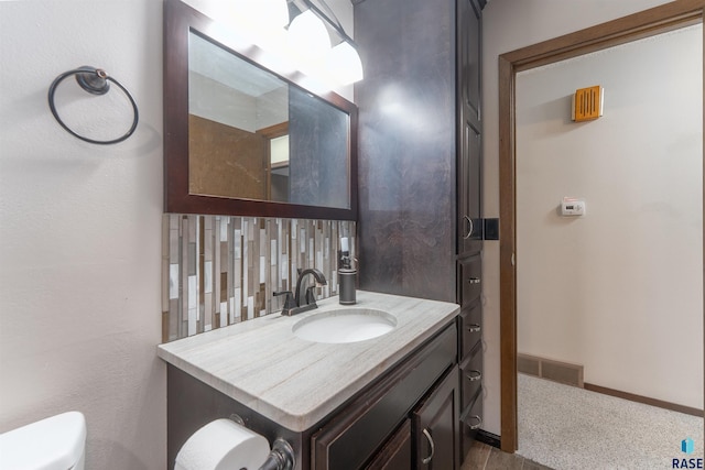 bathroom featuring vanity, visible vents, baseboards, decorative backsplash, and toilet