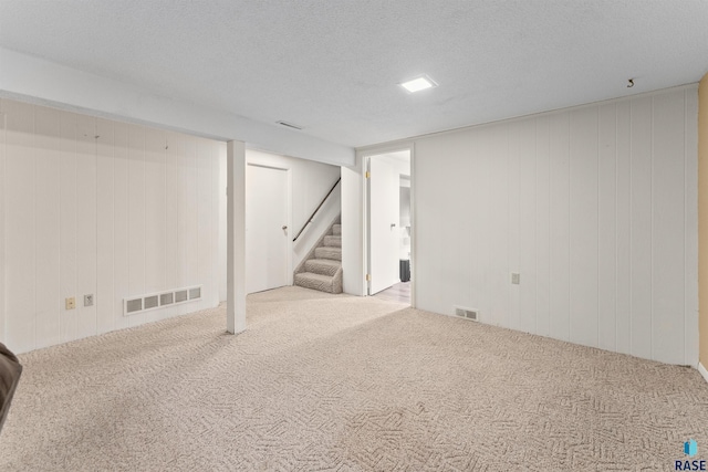 finished below grade area with visible vents, carpet floors, a textured ceiling, and stairs