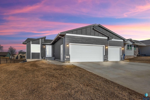 view of front of property with board and batten siding, a front lawn, driveway, stone siding, and an attached garage