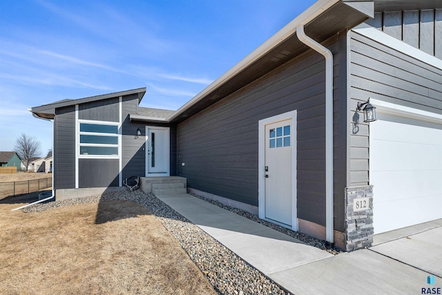 view of exterior entry featuring a garage, board and batten siding, and fence