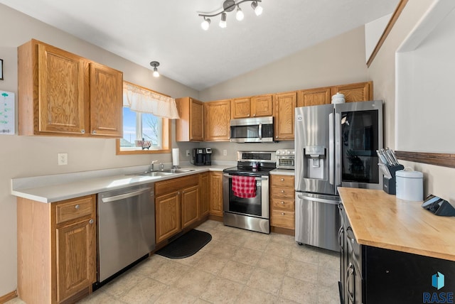 kitchen with brown cabinetry, lofted ceiling, a sink, appliances with stainless steel finishes, and butcher block counters