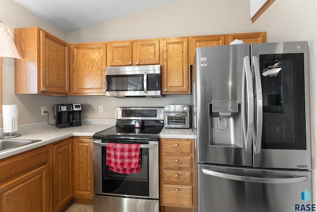 kitchen with lofted ceiling, appliances with stainless steel finishes, a toaster, and light countertops