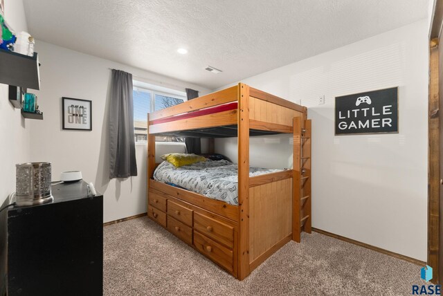 bedroom with baseboards, light carpet, a textured ceiling, and visible vents