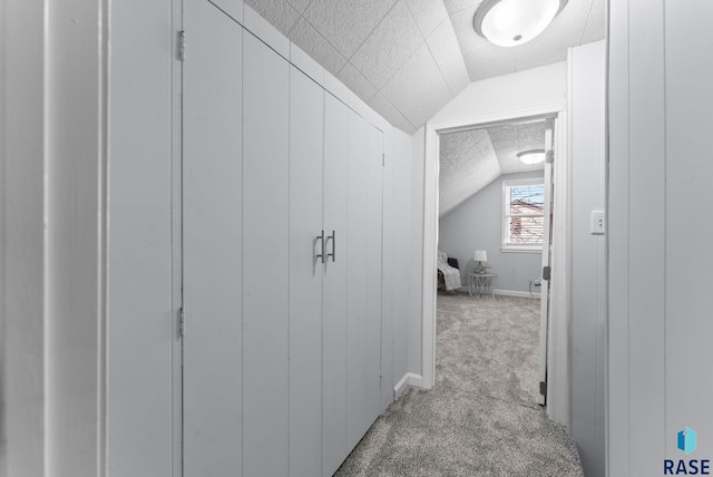 hall with lofted ceiling, light colored carpet, baseboards, and a textured ceiling