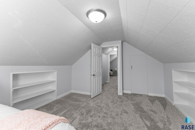 unfurnished bedroom featuring baseboards, lofted ceiling, carpet, and a textured ceiling