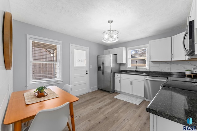 kitchen with light wood finished floors, a sink, appliances with stainless steel finishes, white cabinetry, and a chandelier