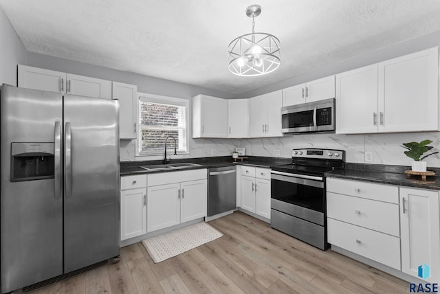 kitchen with decorative light fixtures, light wood-style flooring, stainless steel appliances, white cabinetry, and a sink