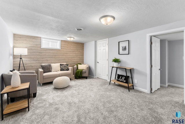 living area with visible vents, a textured ceiling, carpet, wooden walls, and baseboards