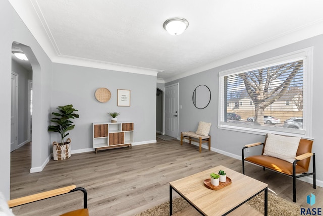 living area with ornamental molding, wood finished floors, arched walkways, and baseboards