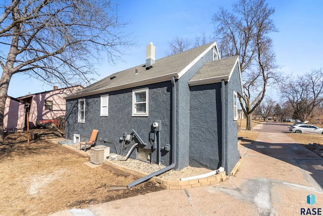 back of house with a chimney, roof with shingles, and stucco siding