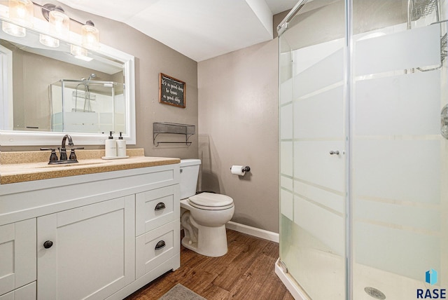 bathroom with toilet, wood finished floors, a shower stall, baseboards, and vanity