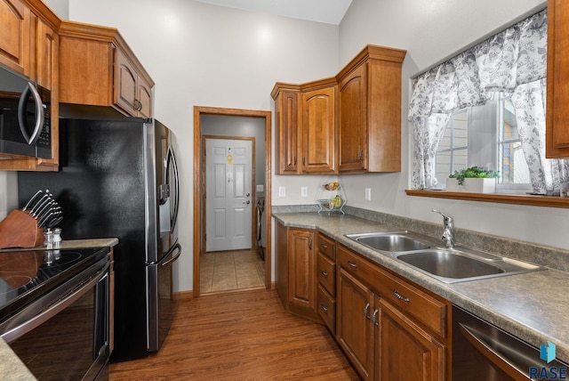 kitchen featuring a sink, stainless steel appliances, wood finished floors, and brown cabinetry