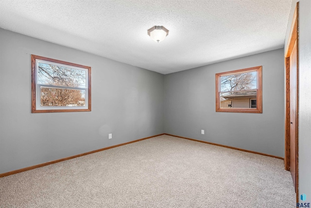 carpeted spare room featuring baseboards and a textured ceiling