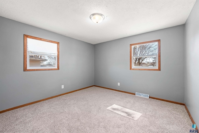 empty room featuring visible vents, carpet floors, a textured ceiling, and baseboards