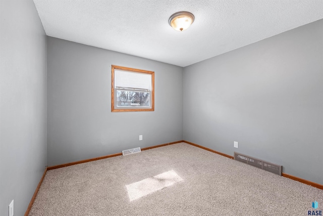 carpeted empty room featuring baseboards, visible vents, and a textured ceiling