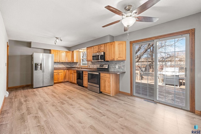 kitchen with dark countertops, backsplash, appliances with stainless steel finishes, and light wood-style floors