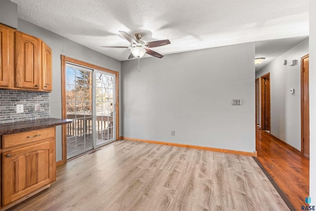 unfurnished dining area with visible vents, baseboards, light wood finished floors, ceiling fan, and a textured ceiling