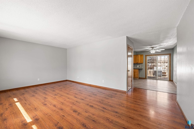 unfurnished room with ceiling fan, a textured ceiling, baseboards, and wood finished floors