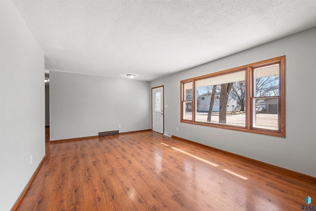 unfurnished room with visible vents, wood finished floors, baseboards, and a textured ceiling