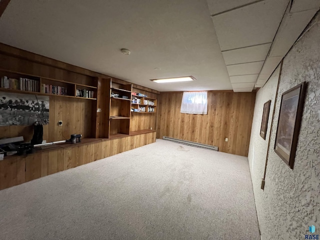 basement featuring wooden walls, baseboard heating, and carpet floors