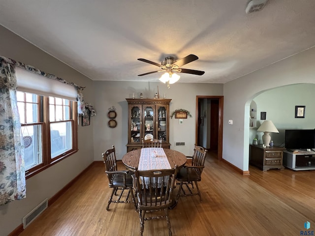 dining room with visible vents, a ceiling fan, wood finished floors, arched walkways, and baseboards