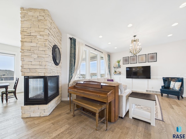 living room featuring a stone fireplace, recessed lighting, wood finished floors, and a chandelier