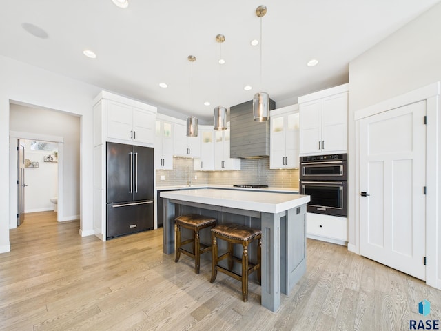 kitchen featuring backsplash, wall chimney range hood, double wall oven, high end black refrigerator, and gas cooktop