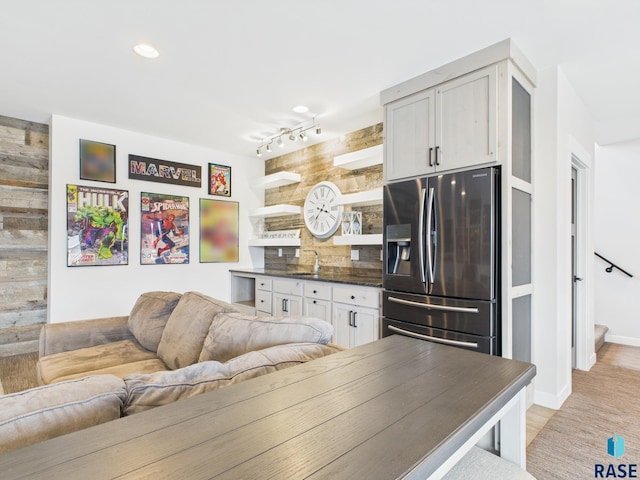 living room featuring light wood-style flooring, rail lighting, baseboards, and wood walls