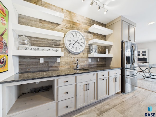 kitchen featuring open shelves, dark stone counters, a sink, track lighting, and stainless steel refrigerator with ice dispenser