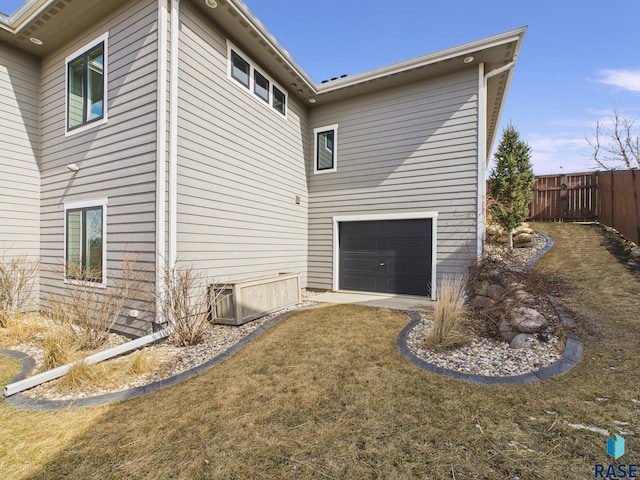 view of home's exterior featuring an attached garage, fence, and a lawn