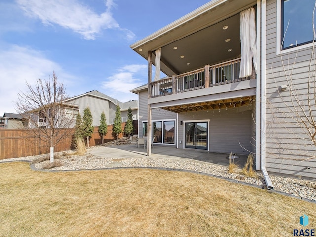 rear view of property featuring a balcony, a lawn, a patio, and fence