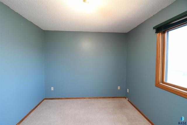 empty room with light colored carpet, a textured ceiling, and baseboards