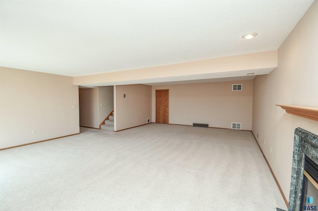 unfurnished living room with stairs, visible vents, a high end fireplace, and light carpet