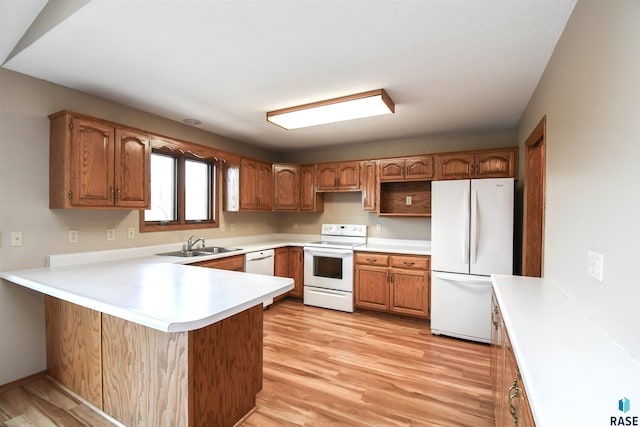 kitchen with white appliances, light wood-style floors, a peninsula, and a sink