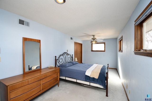 bedroom with visible vents, a textured ceiling, baseboards, light colored carpet, and ceiling fan