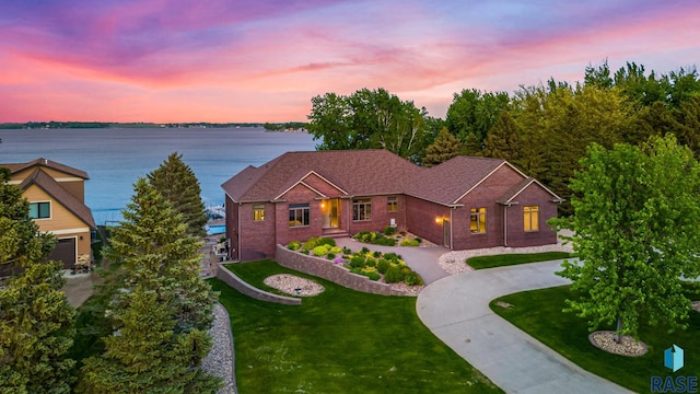 view of front of home featuring concrete driveway, a front lawn, and a water view