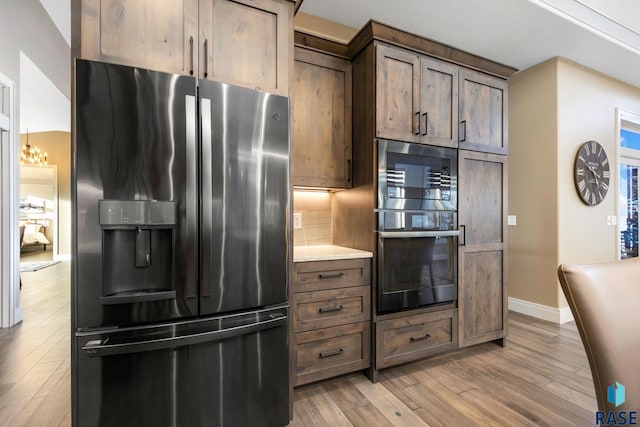 kitchen featuring baseboards, light wood finished floors, double wall oven, light countertops, and stainless steel fridge