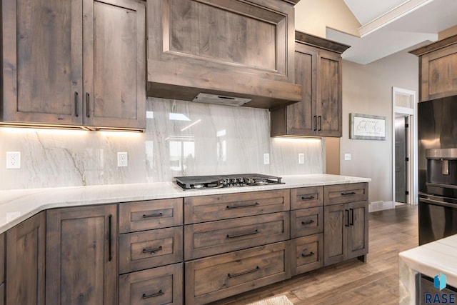 kitchen featuring refrigerator with ice dispenser, custom range hood, tasteful backsplash, wood finished floors, and stainless steel gas cooktop