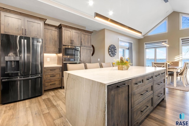 kitchen with light wood-type flooring, built in microwave, tasteful backsplash, and stainless steel fridge with ice dispenser